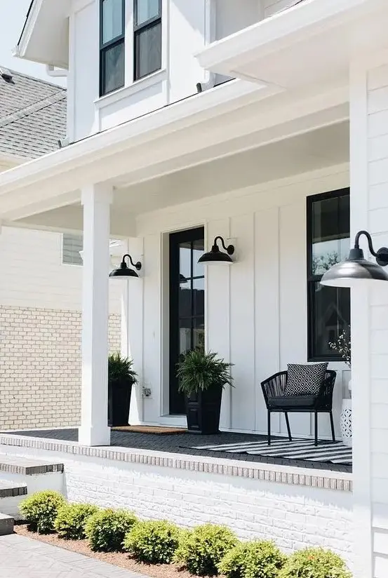 a stylish monochromatic porch with a black chair, a white side table, some cotton, black planters with ferns and sconces