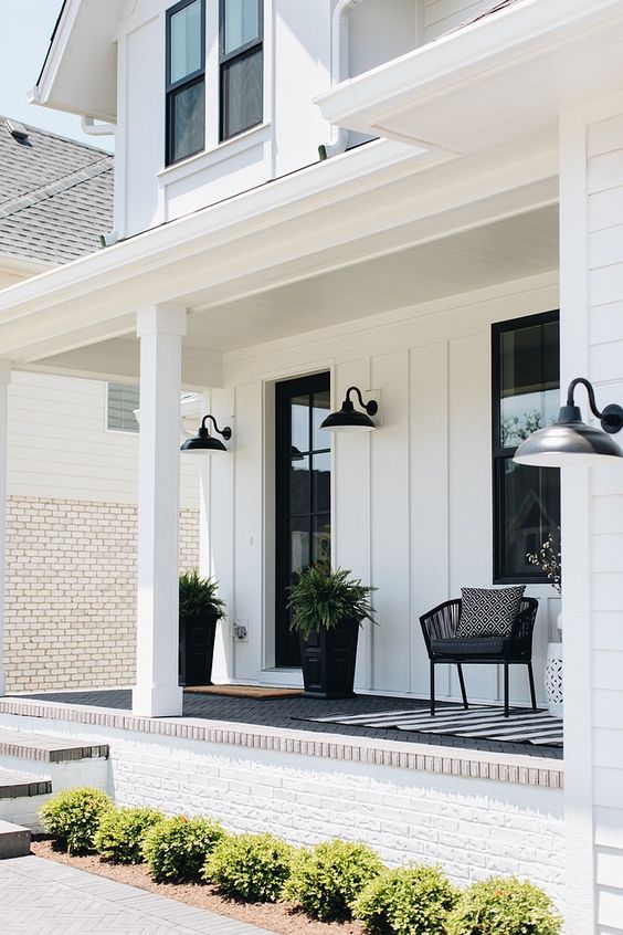 a stylish monochromatic porch with a black chair, a white side table, some cotton, black planters with ferns and sconces