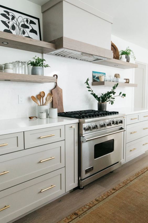 a stylish neutral kitchen in creamy and dove grey cabinets, wooden floating shelves and a white hood