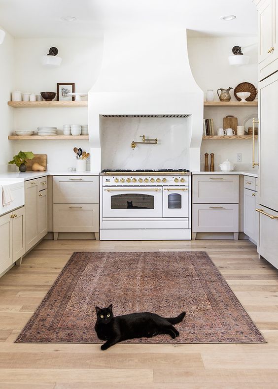 a stylish neutral kitchen with dove grey cabinets, a large white hood, a white cooker, built-in shelves and a printed rug