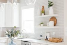 a stylish white and dove grey kitchen with subway tiles, simpel cabinets, pendant lamps and floating shelves