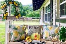 a summer farmhouse porch with a hanging bench, bright citrus print pillows, a citrus wreath and some drinks on a tray