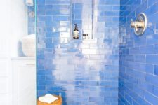 a super bright blue bathroom with subway tiles, mosaic hex tiles on the floor and a wooden stool