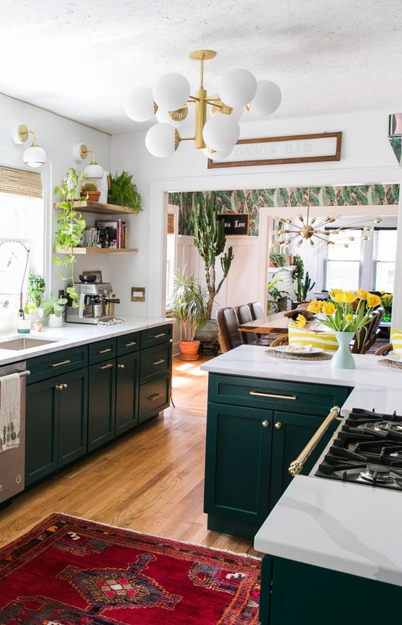 a super catchy boho kitchen with hunter green cabinets, white countertops, gold handles and open shelving