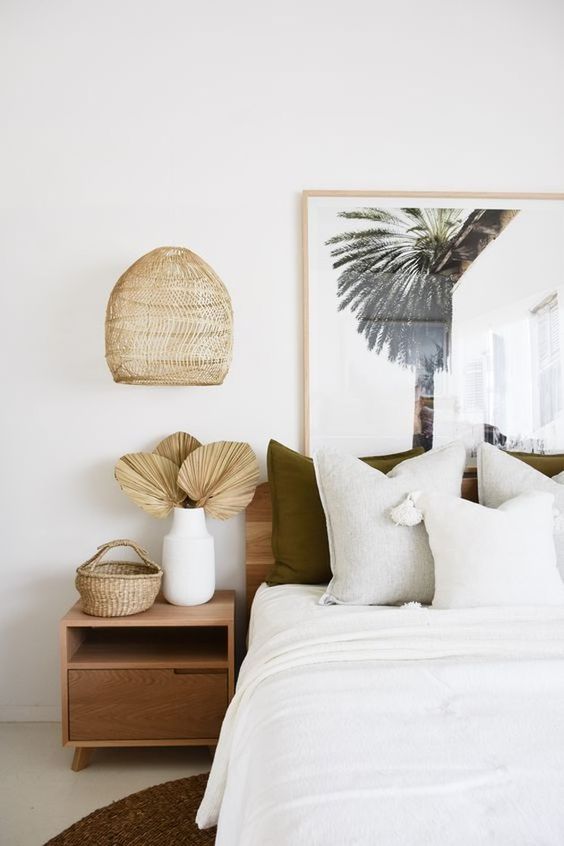 a super neutral tropical bedroom with wooden and plywood furniture, a tropical artwork and wicker touches and dried fronds