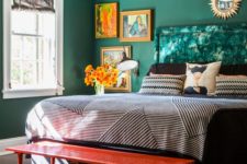 a vibrant bedroom with green walls, a green upholstered bed, a gallery wall, catchy lamps and a red bench