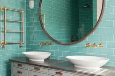 a vintage bathroom clad with turquoise tiles, a large vintage vanity, white sinks, a round mirror and gold fixtures for a chic look