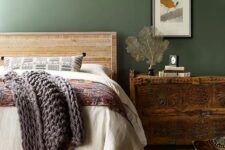a vintage bedroom with green walls, a rough wooden bed with printed bedding, a dark-stained dresser, a chair and a jute rug