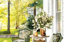 a vintage-inspired summer porch with green wicker furniture, floral upholstery, a vintage table and lots of blooms
