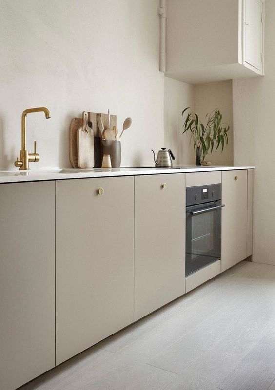 a warm neutral minimalist kitchen with sleek lower cabients, one upper, white countertops and brass touches
