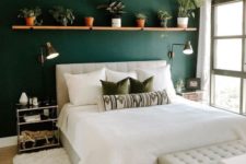 a welcoming boho bedroom with a forest green wall, neutral furniture, a shelf with potted greenery