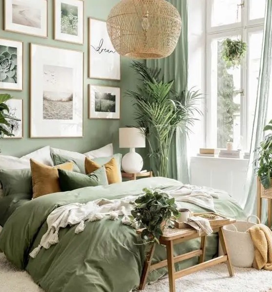 a welcoming sage green bedroom with a bed with sage bedding, a gallery wall, a woven pendant lamp and a wooden bench