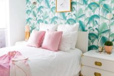 a welcoming tropical bedroom with a tropical leaf wall, white and gold furniture, pink bedding and touches of gold