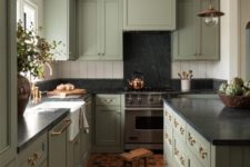 an English cottage kitchen in pale green, with black stone countertops and touches of brass and copper