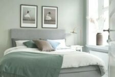 an airy Scandinavian bedroom with sage green walls, a grey upholstered bed with green and neutral bedding, a printed rug