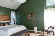 an attic mid-century modern bedroom with green walls, wood and rattan furniture, an oversized lamp and a printed rug