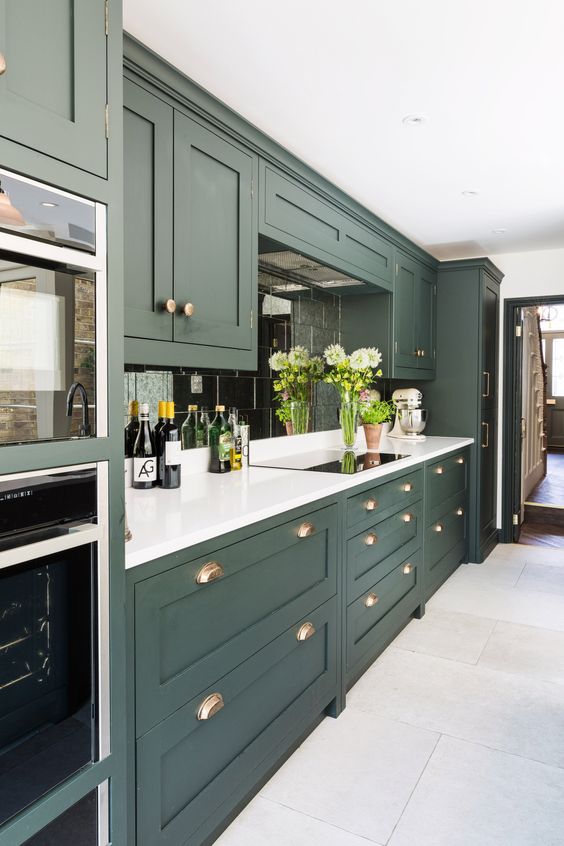 an elegant hunter green kitchen with white countertops, a mirror tile backsplash and touches of brass