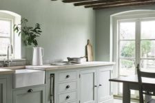 an ethereal modern farmhouse kitchen in pale green, with butcherblock countertops, with wooden beams and much natural light