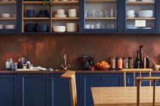 an impressive blue kitchen with a copper backsplash and a rich stained wooden countertop feels refined and vintage-inspired