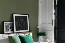 an olive green bedroom with emerald and white bedding, a ledge with artwork and a green table lamp