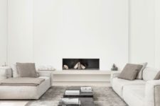 an ultra-minimal living room in neutrals, with a built-in fireplace, neutral furniture, black tables and a grey rug
