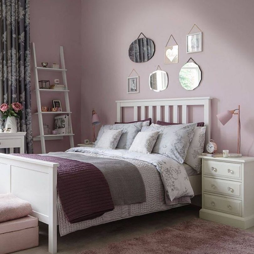 A cozy and romantic bedroom with lilac walls, a mirror gallery wall, purple and floral bedding and neutral furniture