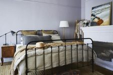 16 a vintage-inspired bedroom with lilac walls, a black forged bed, wooden nightstands, a fireplace and bold artworks