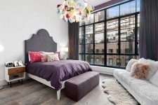 22 a stylish bedroom with a grey statement bed, white furniture, a colorful scale chandelier and pillows plus purple and grey textiles