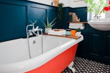 25 an elegant vintage-inspired bathroom with mosaic tiles on the floor, black paneling and an orange bathtub plus potted greenery