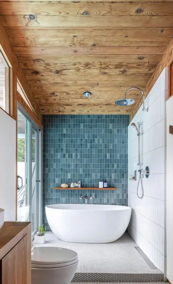 a beautiful coastal bathroom with a wooden ceiling, a blue skinny tile wall, penny ones on the floor, a tub and a glazed wall