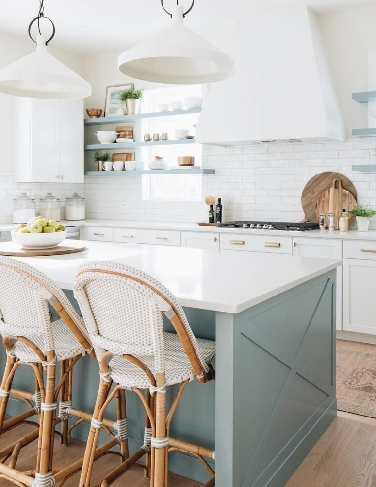 a beautiful coastal kitchen with white cabinets, light blue shelves and a matching kitchen island, rattan chairs and touches of gold
