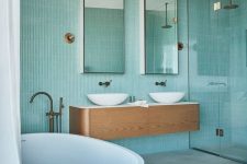 a beautiful seaside bathroom clad with turquoise skinny tiles, a floating vanity and a round tub plus skinny mirrors