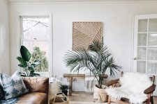 a boho tropical living room in neutrals, with a leather sofa, a fur chair, a wooden bench, baskets and potted plants