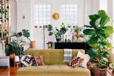 a boho tropical space with a green sofa, boho pillows, lots of potted plants and a printed rug