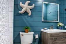a bold coastal bathroom with navy shiplap walls, a timber vanity, white appliances, a starfish decoration and sea-inspired sconces