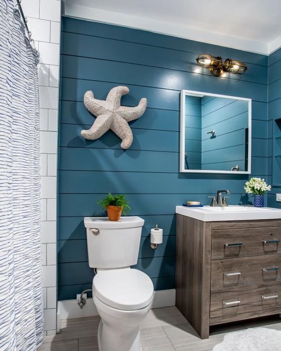 a bold coastal bathroom with navy shiplap walls, a timber vanity, white appliances, a starfish decoration and sea-inspired sconces
