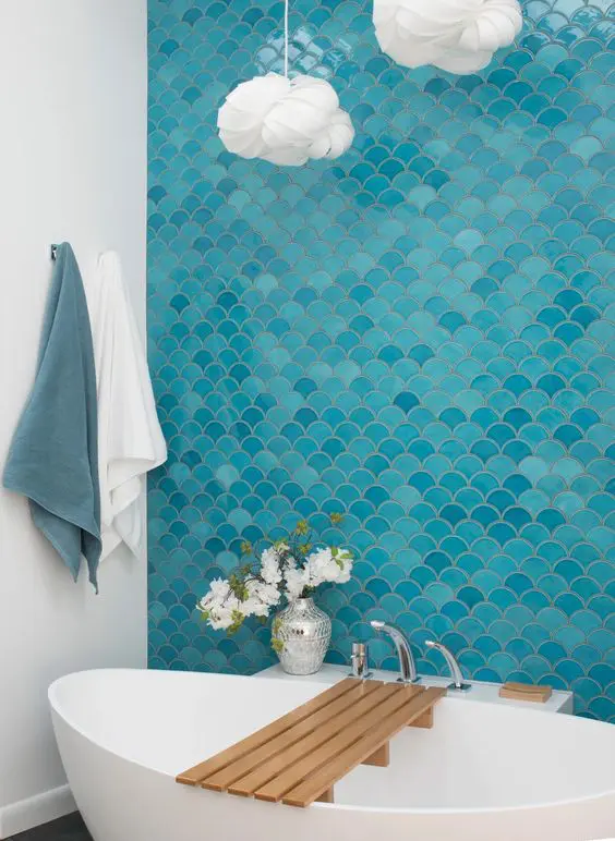 a bold modern bathroom inspired by the sea, with a blue and turquoise fish scale tile wall, an oval tub, cloud-like pendant lamps