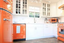a bold modern kitchen with white and orange cabinets, a sunburst chandelier and an orange fridge is cool