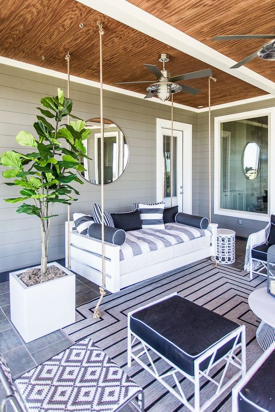 a bold nautical porch with a suspended upholstered daybed, white metal furniture and navy textiles, a potted tree