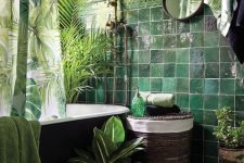 a bold tropical bathroom with green walls, green glazed tiles, a black tub, potted greenery and plants, green towels