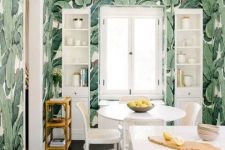 a bold tropical kitchen with banana leaf wallpaper, white furniture and a dining set with rattan chairs