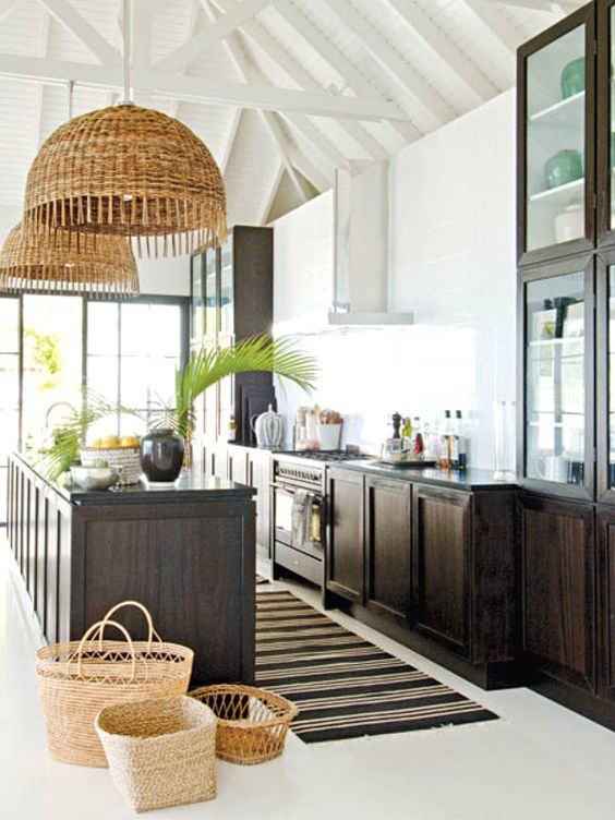 a bold tropical kitchen with white walls, dark stained cabinets, woven pendant lamps and baskets plus tropical leaves