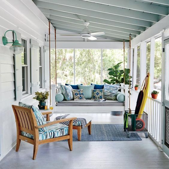 a bright and fun coastal porch with a hanging daybed and a chair with an ottoman, blue pritned textiles and a yellow surf board