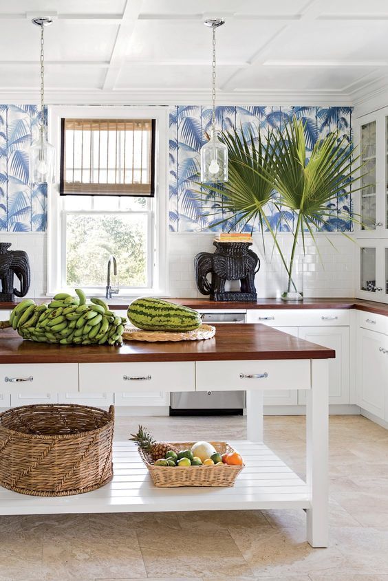 a bright and welcoming tropical kitchen with blue tropical leaf wallpaper, white subway tiles and cabinets plus baskets