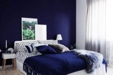 a bright bedroom with a navy accent wall, a white bed with printed blue bedding, simple nightstands and a fluffy pendant lamp