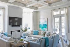 a bright coastal living room with white walls, neutral and light blue furniture, blue pillows, blankets and a turquoise artwork