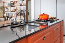a bright modern kitchen with orange furniture, black stone countertops and a metal hood plus vintage fixtures