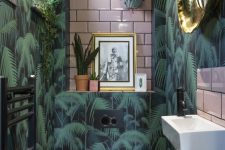 a bright tropical powder room with tropical wallpaper, pink tiles, potted greenery and touches of gold