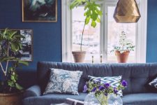 a catchy living room with navy walls, a dark blue sofa, potted plants, copper and brass touches