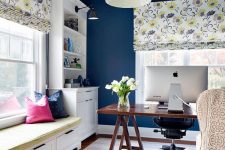 a cheerful navy home office with a trestle desk, floral shades and a printed chair, bright pillows and a mattress